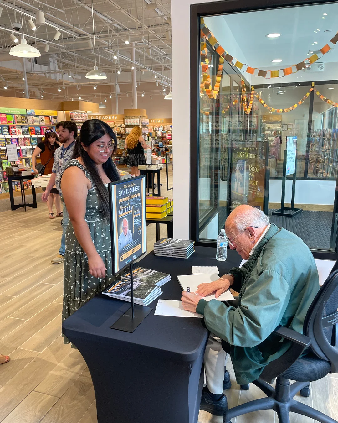 An author signing a copy at a bookshop table while the next reader waits at the side