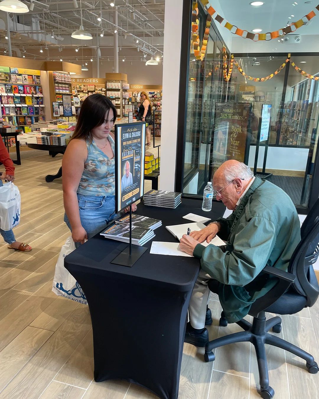 A reader holding a bookshop bag, waiting at the table while the author signs her copy