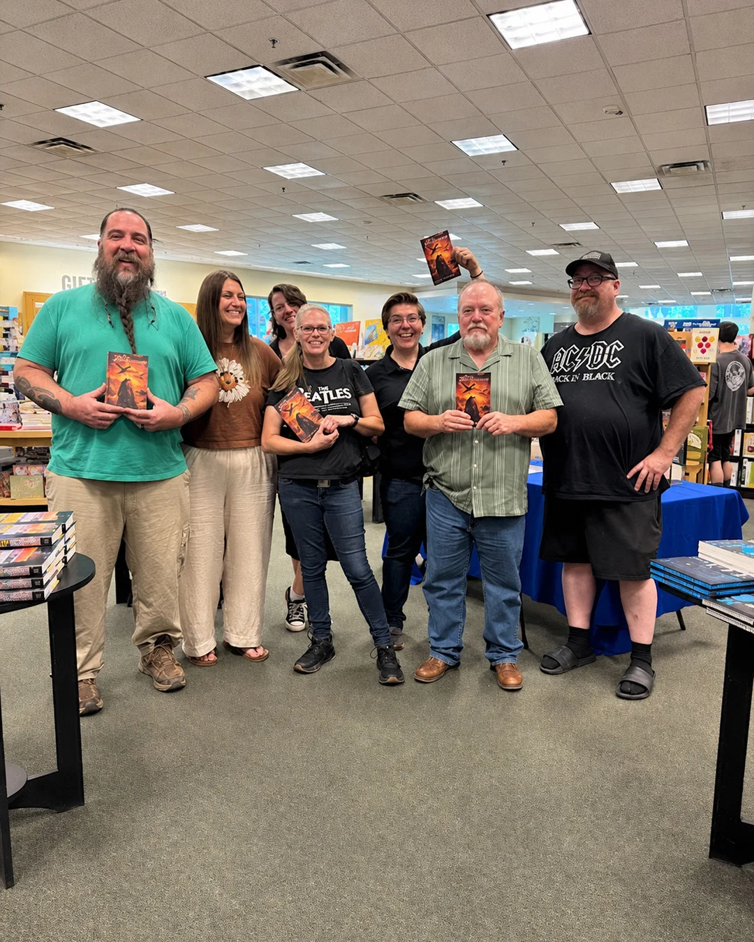 Bookshop staff and readers gathered around the author after a signing, each holding a copy of the book