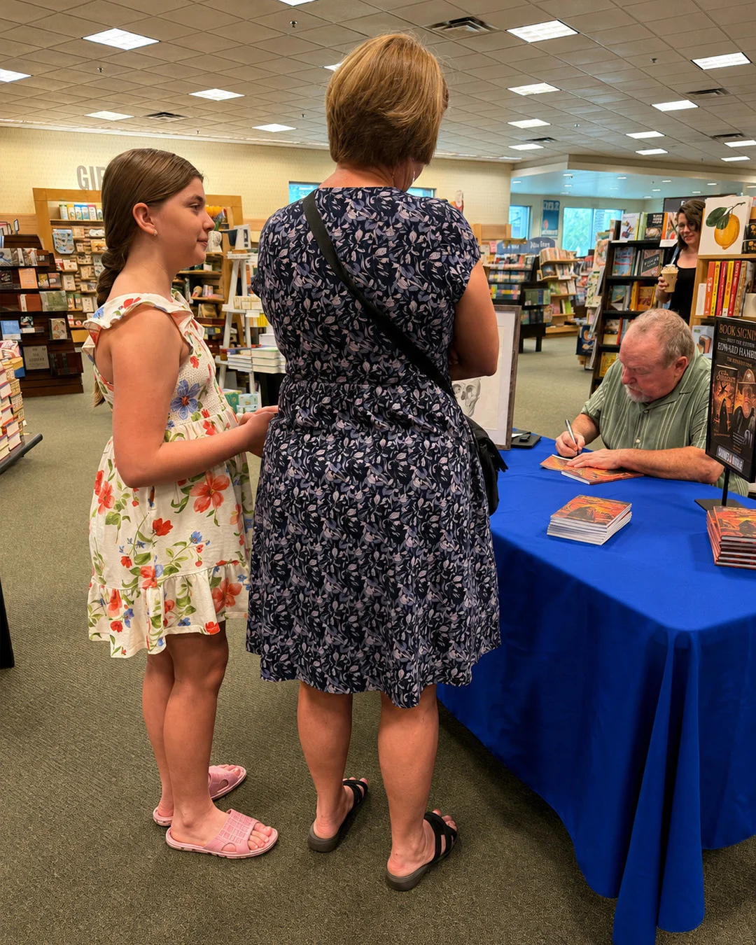 Two customers waiting their turn at the table while the author signs a copy